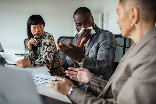 Coworker sneezing into tissue during office meeting