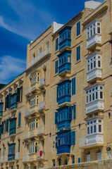 Fototapeta premium Traditional Maltese wooden balconies in Valletta Malta, colorful gallarija on limestone facade against blue sky, architecture