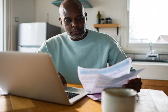 Man reviewing household bills on laptop at home kitchen
