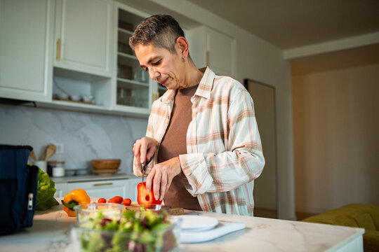 Older woman preparing fresh salad in home kitchen