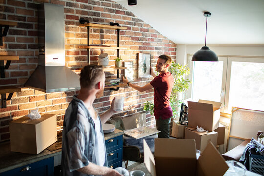Two men unpacking and decorating kitchen in modern brick loft apartment
