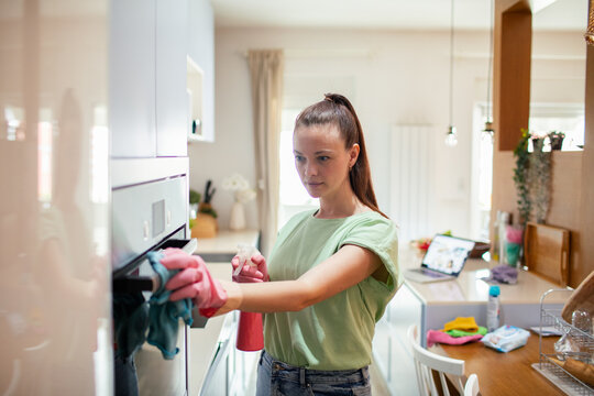 Young woman cleaning oven in modern home kitchen