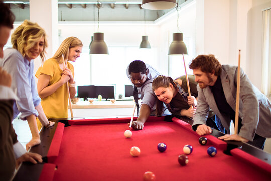 Coworkers playing billiards in modern office break room