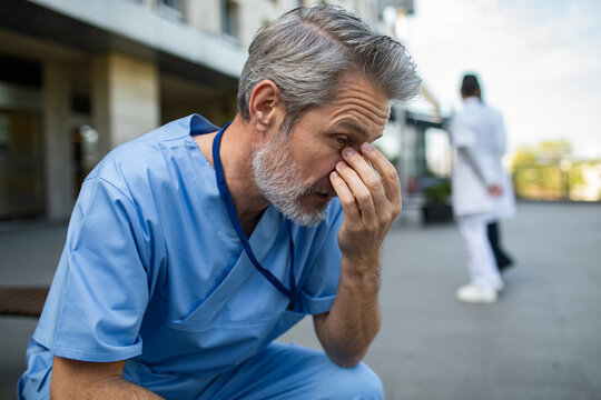 Worried male healthcare worker in scrubs outside hospital