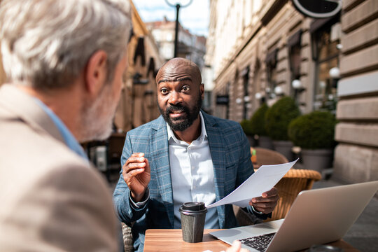 Two businessmen discussing documents at outdoor city cafe