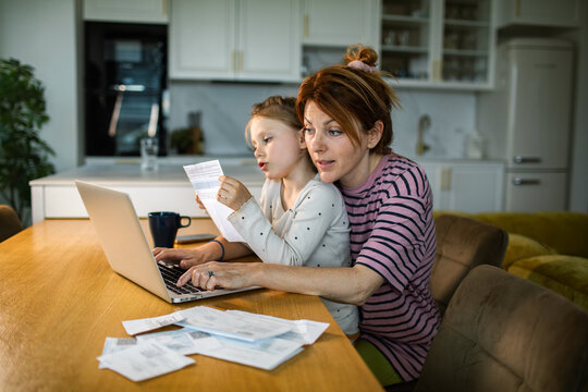 Mother and daughter paying household bills online at kitchen table