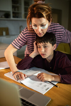 Parent helping tired boy with homework at kitchen table