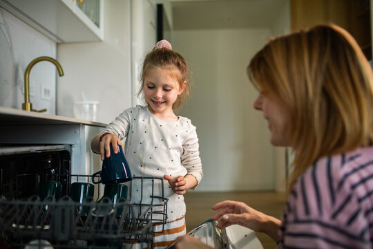 Mother and daughter loading dishwasher in home kitchen
