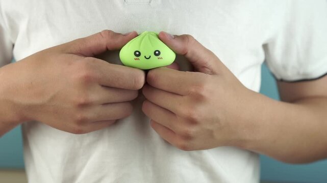 teenager playing with soft green dumpling antistress toy squeezing squishy character for relaxation, close up shot, bright atmosphere, concept of stress relief, sensory fidget game, hobby