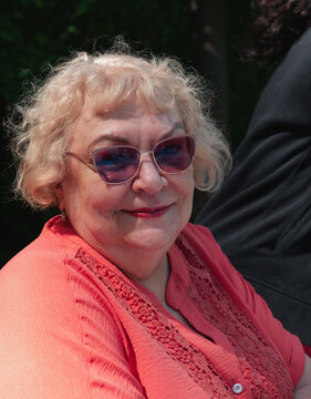 Close up portrait of a senior blonde woman wearing glasses and a coral lace blouse