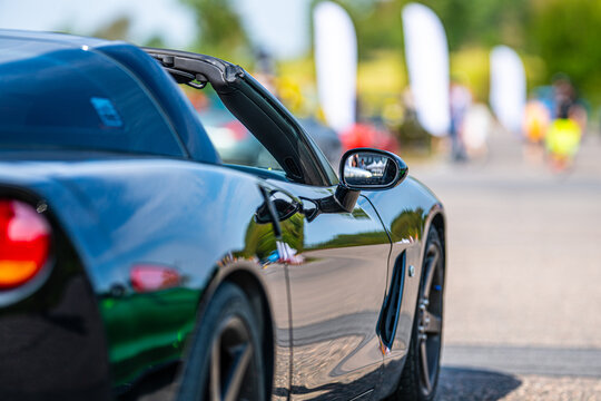 Black sports car with reflective body panel parked at outdoor automotive event.