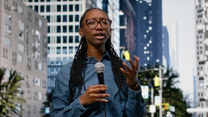 Presenting information on mic, field reporter girl downtown, on city street speaking towards camera, black journalist presenting breaking news reportage with updates, live commentary. © DC Studio