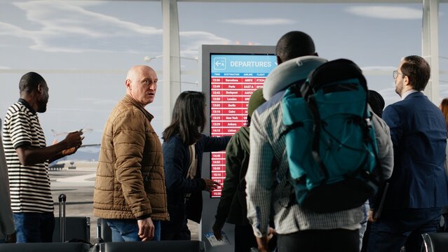 Angry passengers in airport seeing red on departure board screen caused by flight delays, shouting and making phone calls, frustrated traveler upset by flight cancelation on FIDS timetable display.