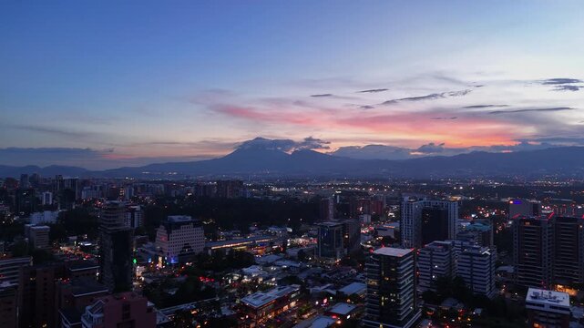 Vista panor&aacute;mica de Ciudad de Guatemala al atardecer con edificios corporativos y volcanes de fondo.