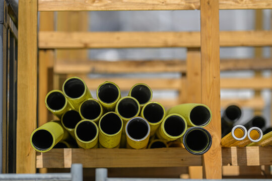 Yellow construction pipes stacked on wooden rack at worksite.