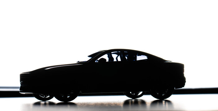 High contrast backlit silhouette of sporty coupe model on reflective surface.