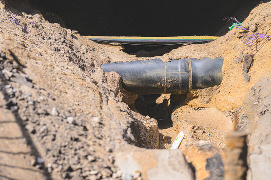 Exposed underground utility pipe crossing sandy trench during infrastructure repair.