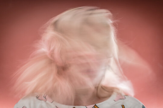 Blurred motion portrait of woman with flowing blonde hair against red background.