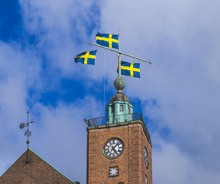 Historic brick clock tower flying Swedish flags under cloudy sky.