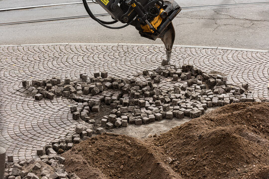 Street construction work removing cobblestone pavement with machinery.