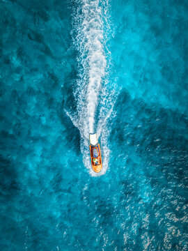 Aerial top down view of orange jet ski moving fast in turquoise ocean water in Mallorca, Spain. Drone view of watercraft speed boat with white foam trail, blue sea, summer travel vacation landscape