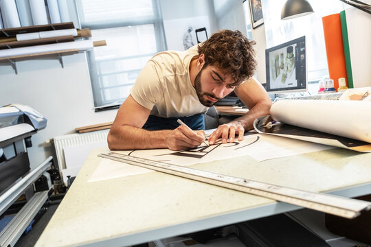 A print shop worker is preparing vinyl cutouts for application, carefully arranging them on transfer film. The process is clean and precise, focused on readying the design for final installation.