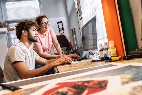 Two colleagues in a print shop work together on preparing a branding project for production. They review designs and print materials, making sure everything is ready before printing.