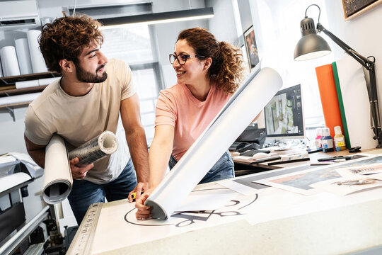Two colleagues in a print shop work together on preparing a branding project for production. They review designs and print materials, making sure everything is ready before printing.