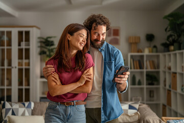 Obraz premium Happy couple looking at smart phone together at home