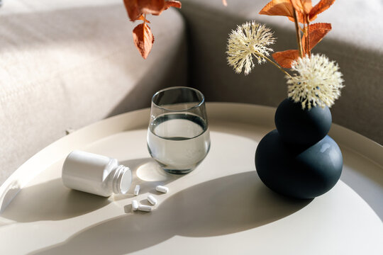 Pill bottle and glass of water on table with flowers in room for health care routine