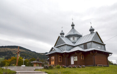 Obraz premium Traditional wooden Church of the Ascension in Bukovets village with dark timber walls and a tiered metal roof. It features three prominent domes topped with crosses against a cloudy, overcast sky
