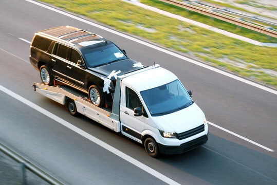 Tow Truck Transporting Second-Hand Used Black SUV Car on Highway, The Concept of Pre-Owned Vehicle Relocation