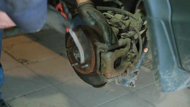Auto mechanic inspecting a brake disc and wheel hub with the wheel removed during tire replacement in a repair shop, ensuring vehicle safety, brake condition and preventive maintenance.