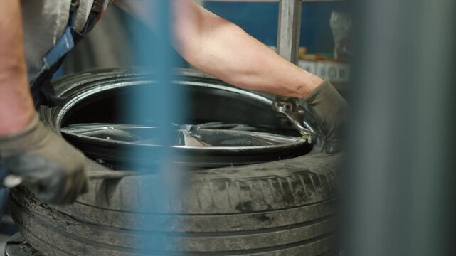 Professional auto mechanic using a tire changing machine to mount or dismount a rubber tire on a wheel rim during seasonal maintenance service in a professional workshop with special equipment