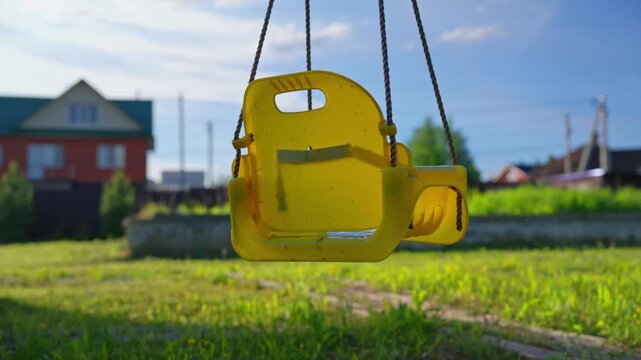 Empty playground swing gently moving in a residential neighborhood, symbolizing childhood, family life, suburban living and quiet outdoor recreation on a sunny day.