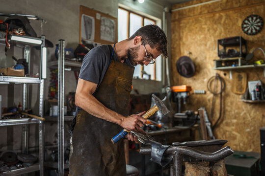 Artisan man crafting metal in his workshop using hammer