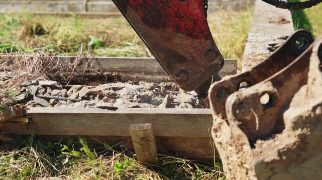 Heavy machinery with a hydraulic breaker attachment powerfully smashes and demolishes a reinforced concrete foundation, sending dust and debris flying during excavation work on a construction site