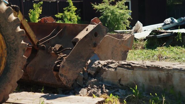 Powerful excavator bucket breaking and crushing old concrete structure on a construction site. Heavy equipment machinery performing demolition work, dismantling a reinforced concrete beam in summer