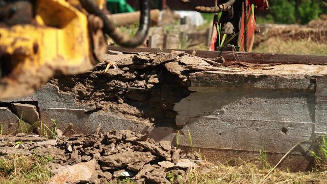 Close-up of damaged concrete foundation edge with soil, rubble and demolition machinery nearby, showing structural removal, site cleanup and residential preparation.