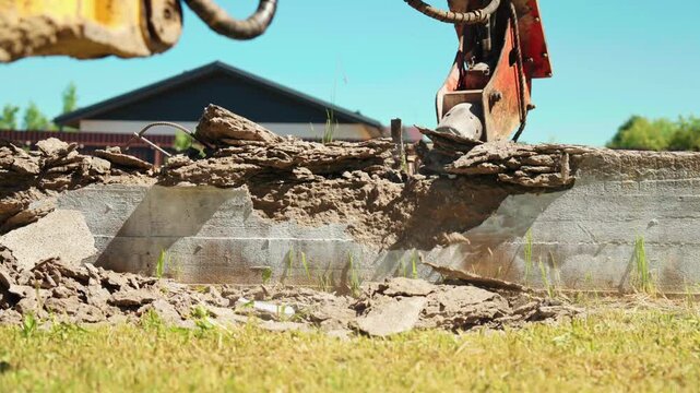 Heavy machinery with a hydraulic breaker attachment powerfully dismantling an old reinforced concrete foundation, sending dust and debris flying during a demolition project on a construction site