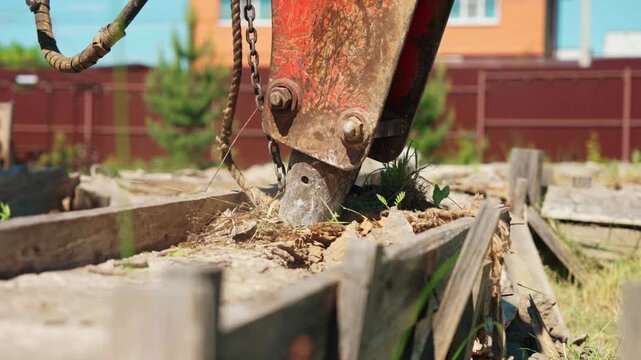Powerful hydraulic breaker attached to an excavator arm destroying an old concrete foundation at a construction site. Heavy machinery dismantling a reinforced concrete structure outdoors