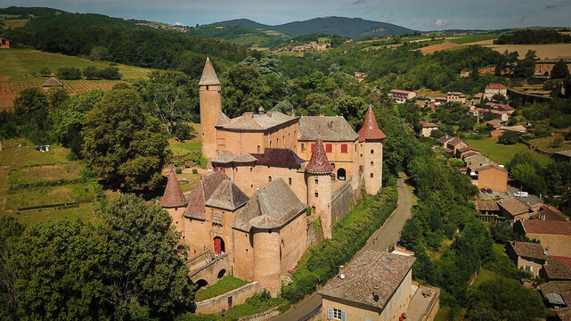 Aerial view of the historic Chateau de Jarnioux surrounded by lush greenery, rolling hills, and stone buildings in Porte des Pierres Dorees, Auvergne-Rhone-Alpes, France.