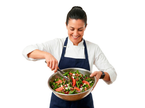 Smiling female chef in uniform prepares a fresh gourmet salad with grapefruit and nuts in a large metal bowl
