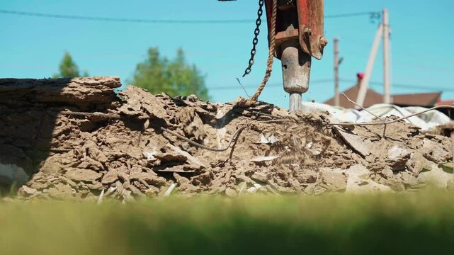 Low angle close-up of hydraulic breaker chipping the top of an old concrete foundation wall, showing dust, rubble and residential site preparation.