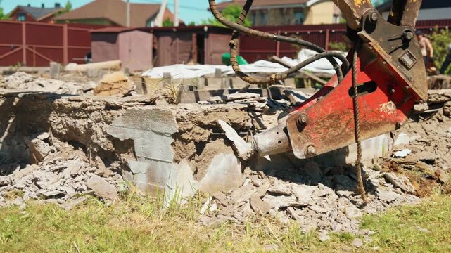 Heavy construction machinery with a powerful hydraulic jackhammer attachment breaking and destroying an old reinforced concrete foundation, creating debris and dust during demolition work