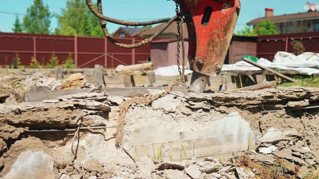 Close-up of hydraulic breaker chipping layered concrete and old wooden formwork on a residential demolition site, showing rubble, rebar and foundation cleanup.