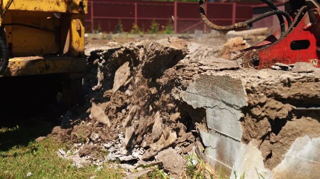 Close-up of old concrete foundation wall collapsing into rubble between demolition machines, showing debris removal, structural teardown and residential site preparation.