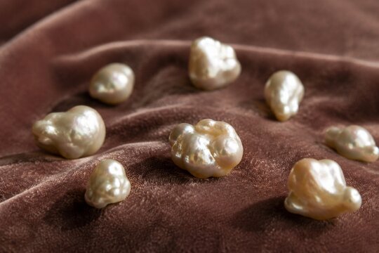 Irregular pearl nodules scattered on velvet fabric in close-up with soft texture and shallow depth.