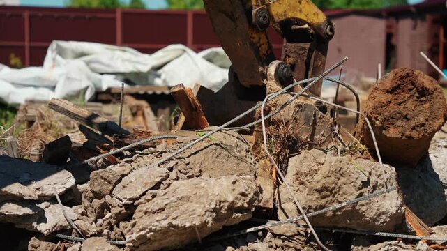 Heavy machinery's hydraulic claw crushing reinforced concrete blocks and bending rebar on a building demolition site