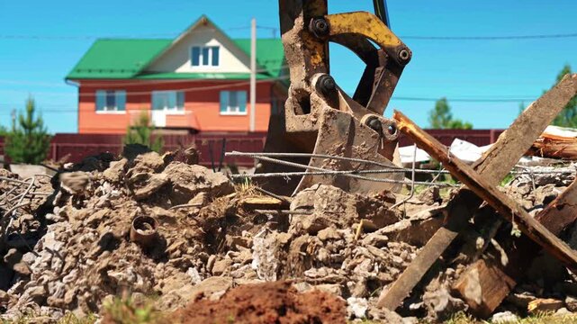 Heavy machinery excavator bucket collecting and removing construction waste from a demolition site. Industrial equipment clearing rubble, concrete, and rebar for new development against a blue sky